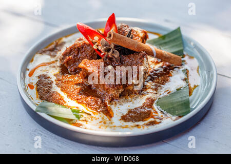 Beef Rendang served on a plate with banana leaf, decorated with red chili and cinnamon stick. Indonesian national cuisine. Stock Photo