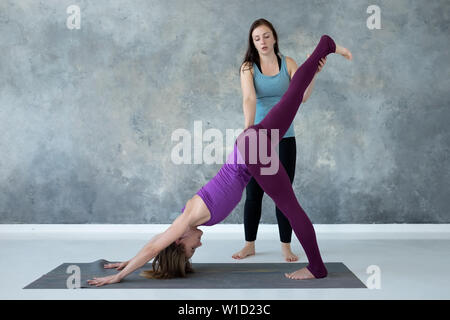Yoga teacher helping her student to stretch muscles holdingher leg Stock Photo
