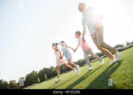 Playing together. Full length of happy and young family of four holding hands, smiling and walking outdoors in park. Family concept Stock Photo