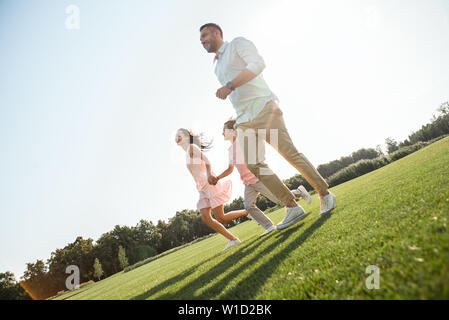 Best moments Side view of happy young family of three holding hands, smiling and walking outdoors in the nature. Family concept Stock Photo