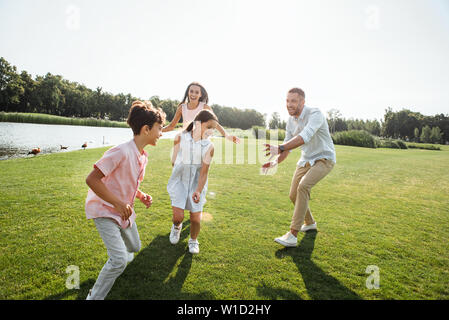 Time for fun. Happy father trying to catch his children and smiling while spending free time with family outdoors in park. Family concept Stock Photo
