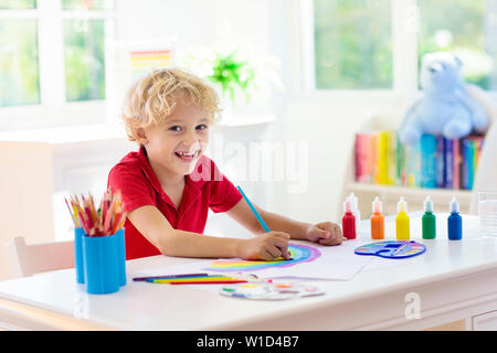 Kids paint. Child painting in white sunny study room. Little boy drawing rainbow. School kid doing art homework. Arts and crafts for kids. Paint on ch Stock Photo