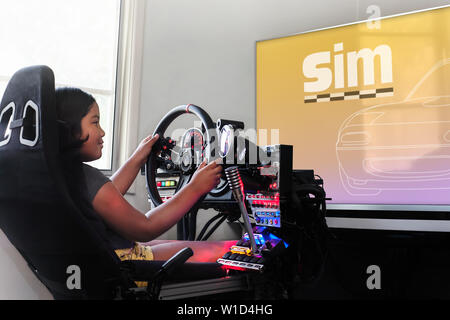 A little girl sitting in a gaming cockpit and holding the race steering wheel to play a racing simulation. Stock Photo