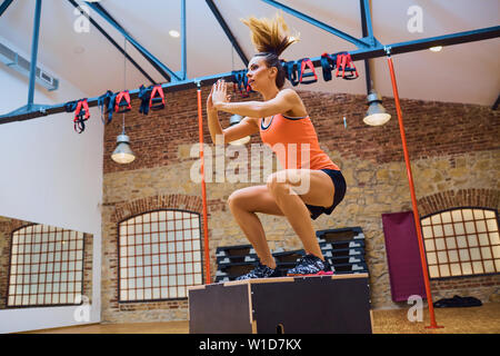 Young woman doing ox jump exercise at gym Stock Photo