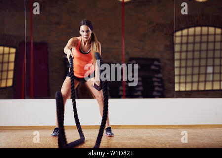 Athletic woman doing battle rope exercises at gym Stock Photo
