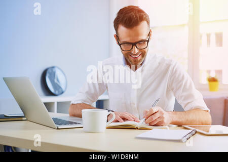 Handsome man working from home office doing notes sitting at desk Stock Photo