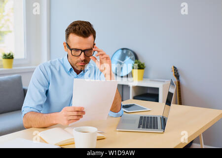 Serious man reading document at home sitting by desk Stock Photo