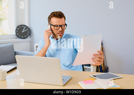 Angry man paying his bills with laptop and  talking on phone at home Stock Photo