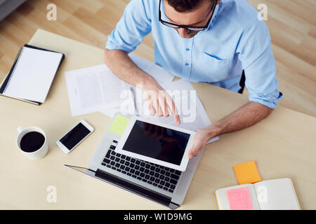 Top view of man using digital tablet sitting at  desk with documents and laptop Stock Photo