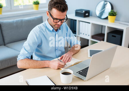 Young man writing in journal while working in home office Stock Photo