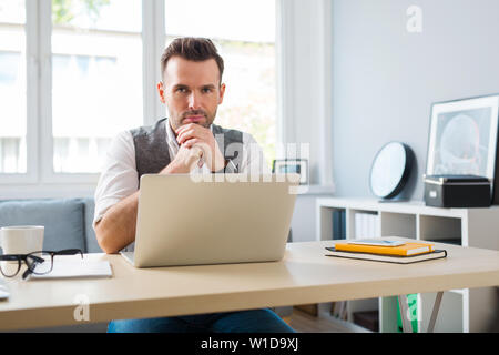 Young designer at home office working on laptop looking at camera Stock Photo