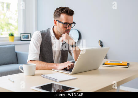 Pensive man working on laptop from home Stock Photo