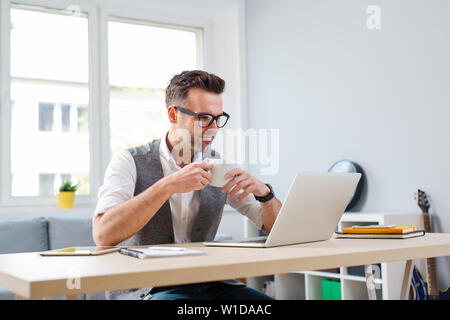 Man working from home on his laptop, drinking coffee Stock Photo