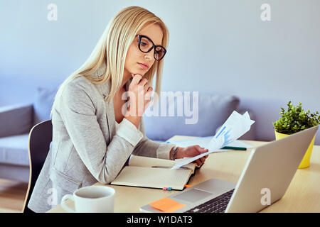Young woman working from home office with laptop and some financial documents Stock Photo