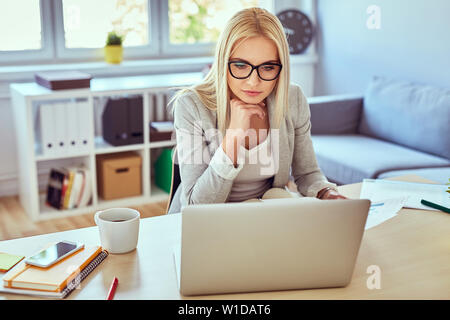 Thoughtful woman working on laptop from home Stock Photo