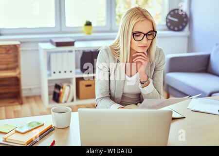 Thoughtful woman reading financail documents while working with laptop from her home office Stock Photo