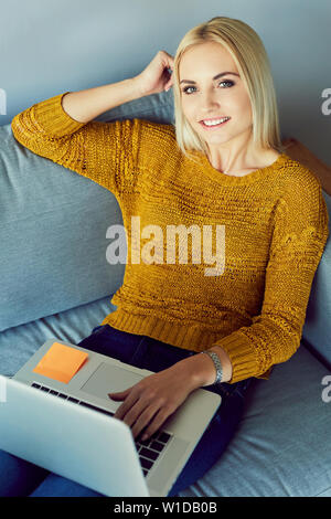 Happy young woman sitting with laptop on sofa Stock Photo