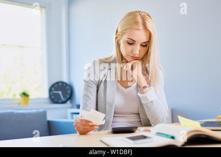 Sad young woman counting bills sitting at desk in home office Stock Photo