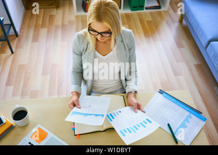 Overhead picture of young business woman looking at documents with financial data sitting by desk at home Stock Photo