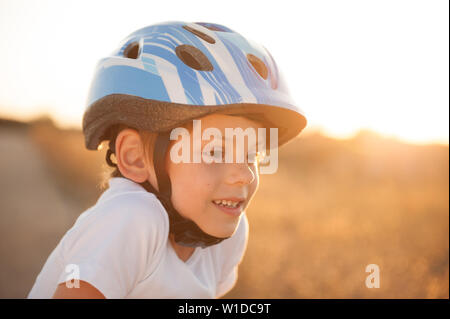 portrait of happy smiling cute little caucasian boy in blue sport helmet and white shirt on summer sunset outdoors Stock Photo