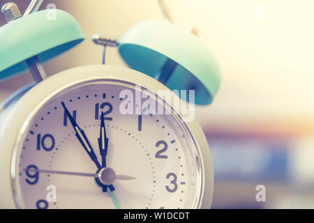 Alarm clock is standing on a grey desk, books in the blurry background Stock Photo