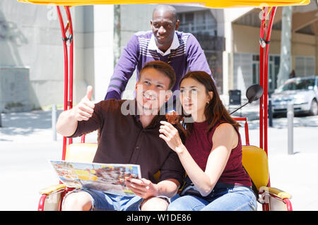 Young girl with boyfriend traveling on rickshaw through city streets, friendly talking with driver Stock Photo