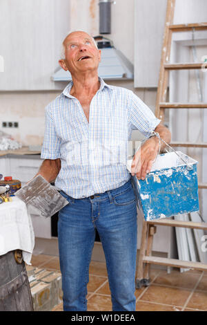 Senior man working on his house overhaul, determining scope of plastering works indoors Stock Photo
