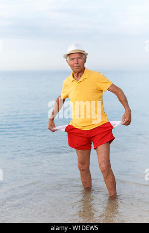 Sad man in headwear shows empty pockets near ocean Stock Photo