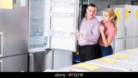 young couple chooses refrigerator in shop of household appliances Stock Photo