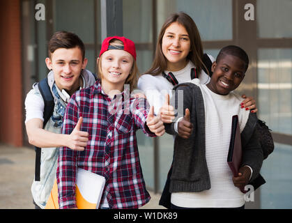 Positive friends with folders and backpacks near college Stock Photo