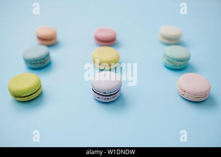 Closeup of delicious sweet French macaroon or macaron biscuits lying in three lines on pastel blue background. Stock Photo