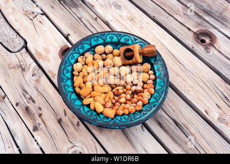 Beautiful Blue ceramic Bowl containing almonds, walnuts and hazelnuts and a nutcracker. Served on a rustic old wooden table. Stock Photo