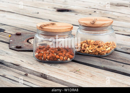 Two glass cans with wood lid containing peeled hazelnuts and walnuts. served on an old rustic cable drum, converted into a table. Stock Photo