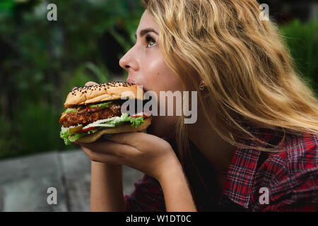 Student consume fast food. Girl bite of very big burger in the garden Stock Photo
