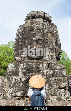 Woman in Bayon Temple looking at stone faces, Angkor Thom, morning light clear blue sky. Buddhism meditation concept, world famous travel destination, Stock Photo