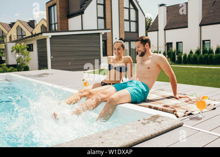 Lovely heteroseksual couple having water resting. Man and woman sitting near water pool and funny splashing water their legs Stock Photo