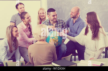 Highschool students having fun with a globe at geography class during a break in a classroom Stock Photo