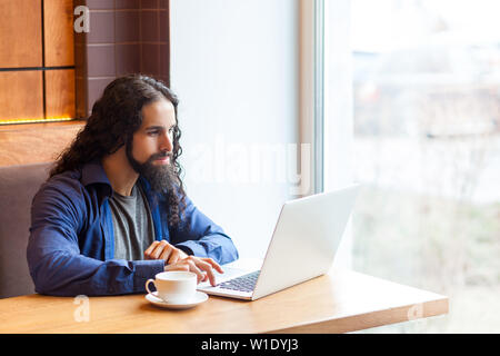 Portrait of handsome intelligence bearded young adult man freelancer in casual style sitting in cafe and searching information for work in laptop, bus Stock Photo