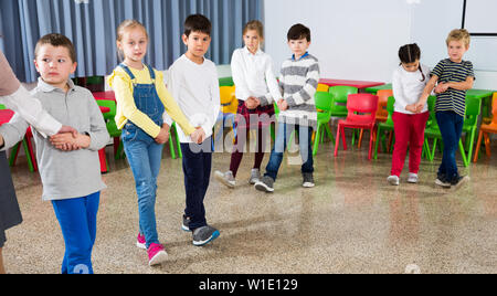 Group of cheerful school kids learning to dance in pairs with their teacher in classroom on recess Stock Photo