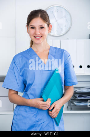 Portrait of young general practitioner in blue overall holding clipboard with medical records Stock Photo