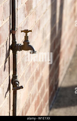 A single spigot or tap or faucet silhouetted against a brick wall in direct sunlight Stock Photo