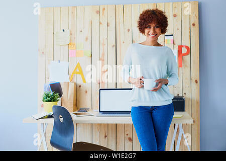 Successful female designer standing by her desk in office with cup of coffee Stock Photo