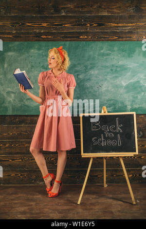 Teacher reading book in classroom. Pretty woman is back to school and reading book at blackboard. Adorable and genius student. Train your brain. Stock Photo