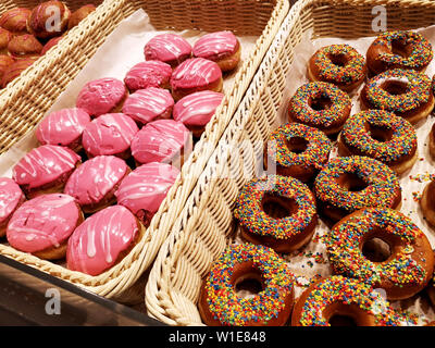 Assorted sweet donuts,  glazed pastries with sprinkles in basket in bakery shop Stock Photo