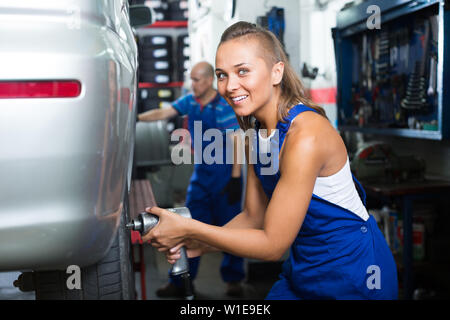 friendly smiling joyful female mechanic  working on car tyre assembling in service station Stock Photo