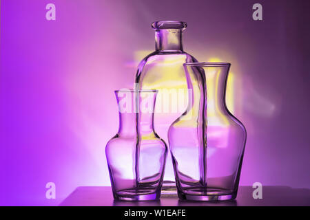 glass transparent tableware - bottles of different sizes, three pieces on a beautiful multi-colored, yellow, lilac and pink, background. very Stock Photo