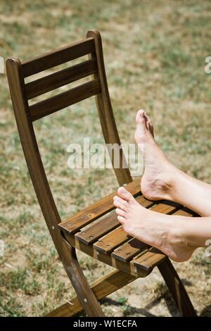 Woman's foot on brown wooden chair outdoor Stock Photo