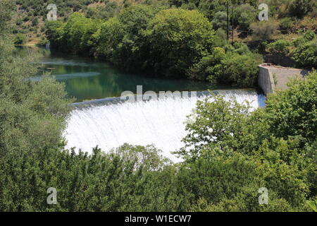 Water spills over the top of Louros river hydroelectric dam in a green forest in Epirus, Greece near the town of Filippiada Stock Photo