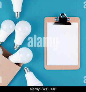 Energy-saving and eco-friendly life in conceptual composition. Creative top view flat lay of LED light bulbs in craft paper shopping bag and clipboard Stock Photo
