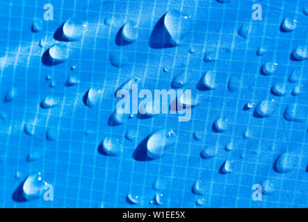 Large drops of water on a blue textile with a waterproof effect. Water-repellent impregnation. Texture drops on the fabric. Stock Photo